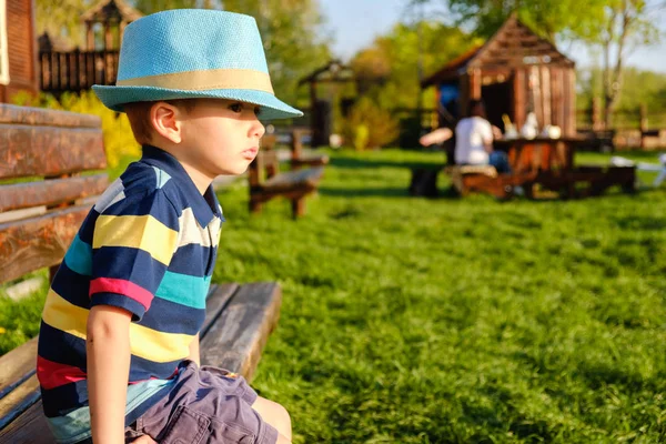 Niño sonriente sentado en un banco del parque con prado verde en el fondo —  Fotos de Stock
