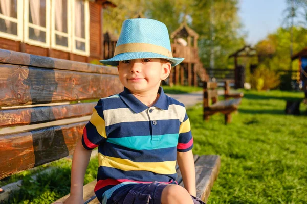 Niño sonriente sentado en un banco del parque con prado verde en el fondo —  Fotos de Stock