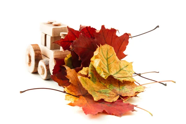 Petit tracteur jouet est chargé de feuilles jaunes tombées contre un blanc. Nettoyage et enlèvement des feuilles tombées — Photo