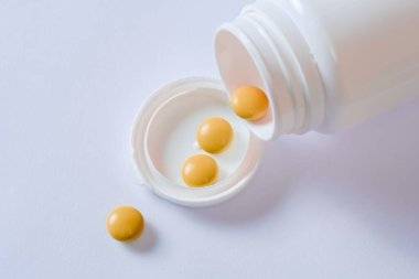 Plastik şişenin yanında bir sürü ilaç duruyor. Haplar ve şişeler beyazdır. Beyaz arkaplanda izole