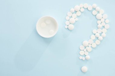 Tıbbi muayene, teşhis ve tedavi kavramlarını mavi arka planda, karışık hapları soru işareti olarak izole et