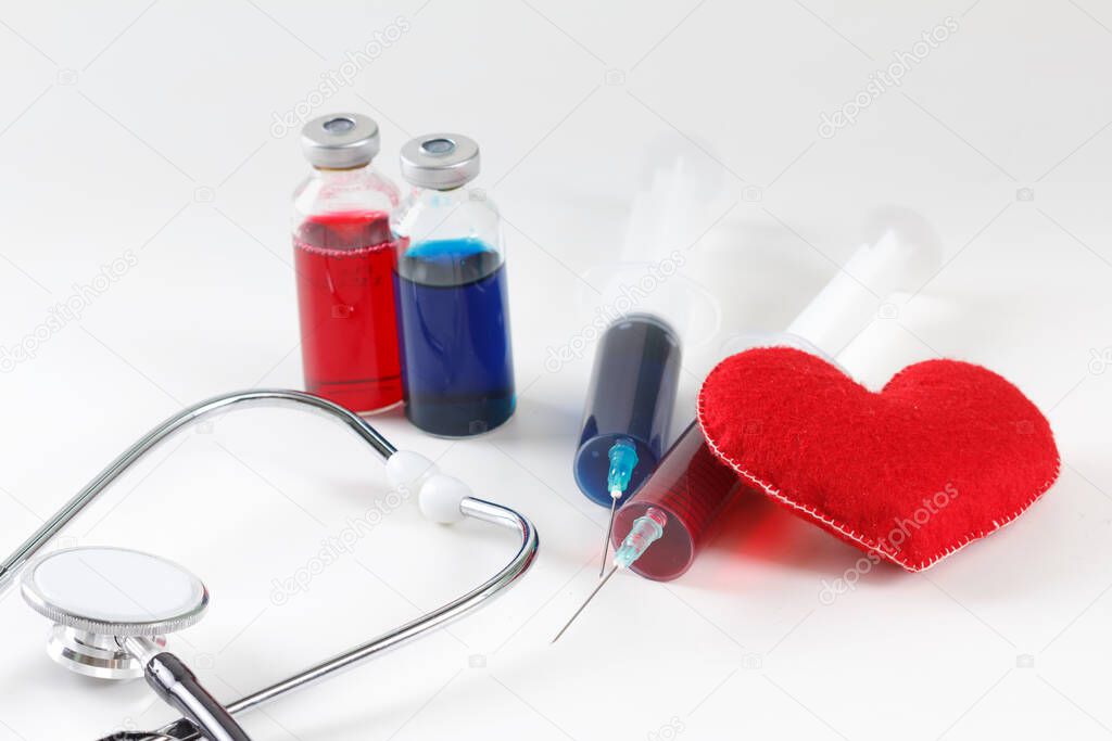 Red heart and a stethoscope on desk with suringe. Medical concept