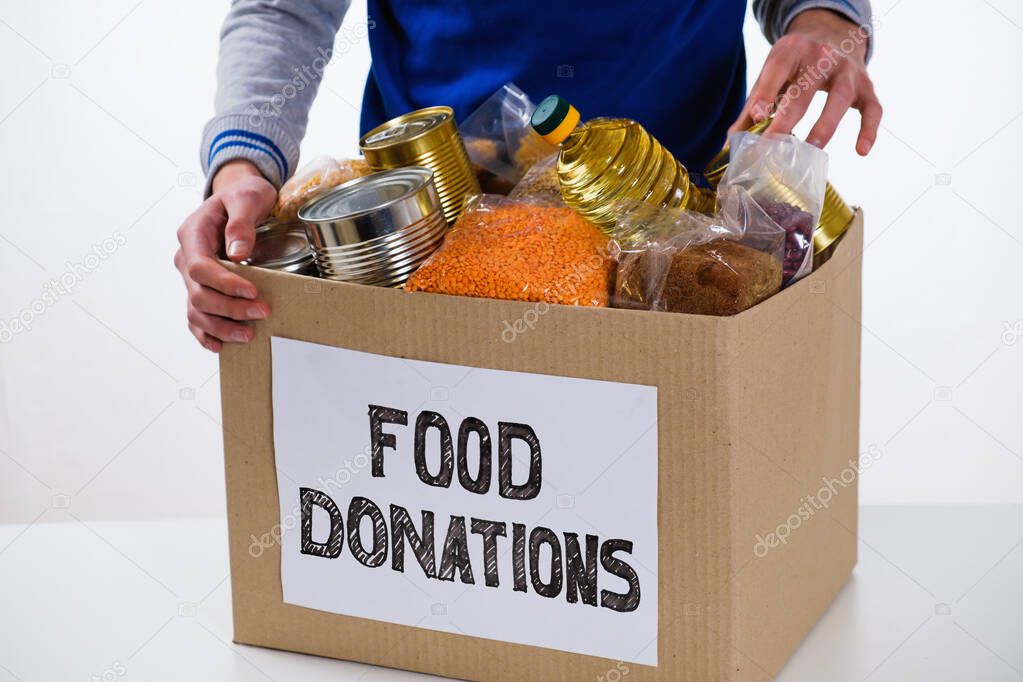 Food in a donation cardboard box, isolated on white background, volunteer fills the box.