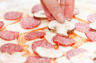 Aşçı mozzarella ve salamın üzerine mantar koyup yakın plan çiğ pizza yapıyor.
