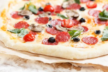 Salamlı, mantarlı, domatesli, mozzarella ve fesleğenli ev yapımı pizza.