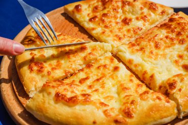 Dört peynirli pizza quattro fromaggi 'yi ahşap bir tahta üzerinde bıçakla kesmek ve mavi arka plan