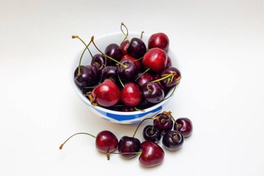 Siyah ve kırmızı kirazlar beyaz arka planda bir tabakta.