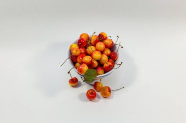 Beyaz zemin üzerinde sarı kirazlar, yukarıdan manzaralı bir tabakta.