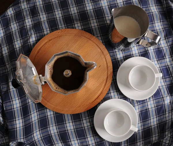 Geysir-Kaffee auf rundem Schneidebrett, eine Kanne Milch und Tassen auf blau karierter Tischdecke — Stockfoto