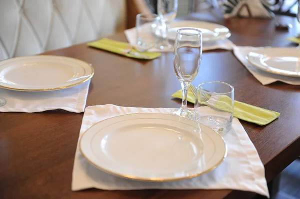 Mesa servida en restaurante. Placas blancas, vasos sobre un paño blanco sobre una superficie de madera — Foto de Stock