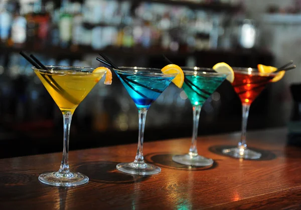 Cuatro cócteles de colores en el bar. Amarillo, azul, verde, rojo. Decorado con una rodaja de limón — Foto de Stock