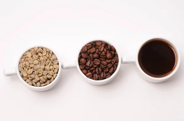 Tres tazas blancas con diferentes etapas de café: frijoles verdes y tostados y bebida preparada — Foto de Stock