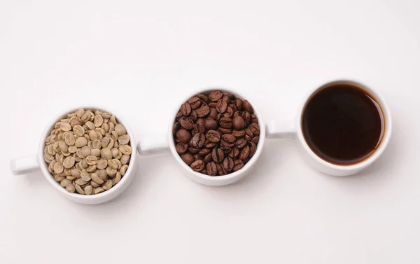 Tres tazas blancas con diferentes etapas de café: frijoles verdes y tostados y bebida preparada — Foto de Stock