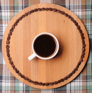 Fincan espresso yuvarlak ahşap tahta üzerinde devre kahve çekirdekleri ile. Ekose arka plan üzerinde