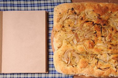 Soğan İtalyan ekmeği ve açık defter metin için boş alan ile. Ekose masa örtüsü ile ahşap tablo