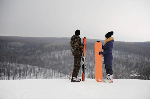 Homem e menina com snowboard e esquis em pé em cima de um fundo monocromático de uma paisagem de inverno — Fotografia de Stock