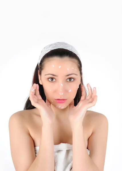 Young long-haired brunettein towel applies the cream to face on a white background — Stock Photo, Image