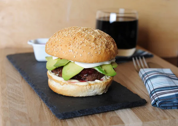 Burger, beer and berry sauce in white gravy boat on a slate base, glass and cutlery served on a wooden board,