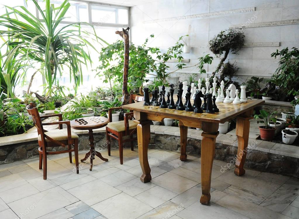Chess table with large chess pieces on the background of greenhouse