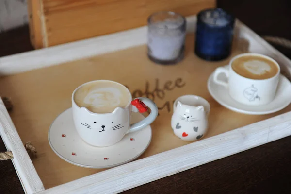 Cappuccino café dans une tasse mignonne en forme de chat. Sur un plateau en bois. Bougies sur le fond — Photo
