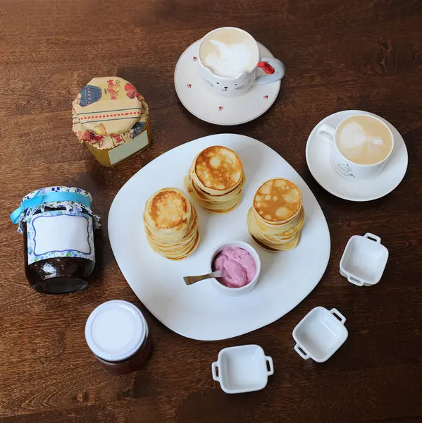 Pancakes with berry sauce on a white plate. Cappuccino in cups, sauce boats, jars of jam. Top view — Stock Photo, Image