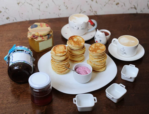 Pancakes with berry sauce on a white plate. Cappuccino in cups, sauce boats, jars of jam — Stock Photo, Image