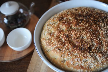 Taze focaccia ekmek seramik formundaki susam ile yuvarlak. Ahşap bir masaya hizmet. Bitkisel çay, su bardağı, reçel