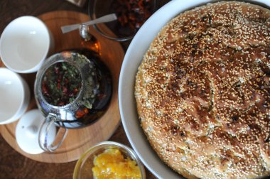 Taze focaccia ekmek seramik formundaki susam ile yuvarlak. Ahşap bir masaya hizmet. Bitkisel çay, su bardağı, reçel