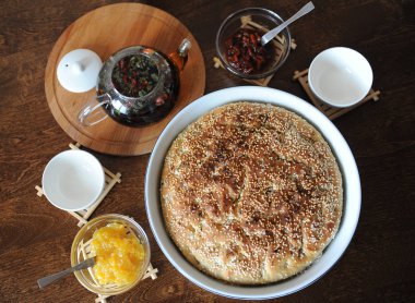 Taze focaccia ekmek seramik formundaki susam ile yuvarlak. Ahşap bir masaya hizmet. Bitkisel çay, su bardağı, reçel