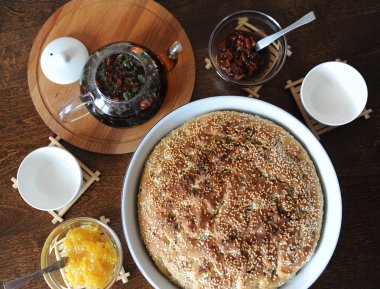 Taze focaccia ekmek seramik formundaki susam ile yuvarlak. Ahşap bir masaya hizmet. Bitkisel çay, su bardağı, reçel