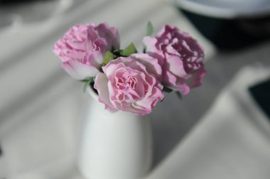 Bir restoranda bir masada küçük bir zarif vazoda narin pembe çiçekler. Doğal güneş ışığı