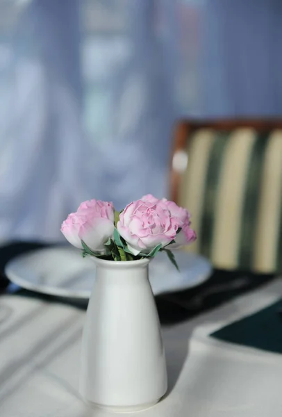 Delicadas flores rosadas en un pequeño jarrón elegante sobre una mesa en un restaurante. Luz solar natural — Foto de Stock