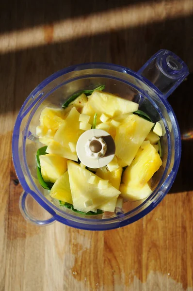 Orange, pineapple, avocado, spinach greens and fresh ginger in the blender bowl, top view