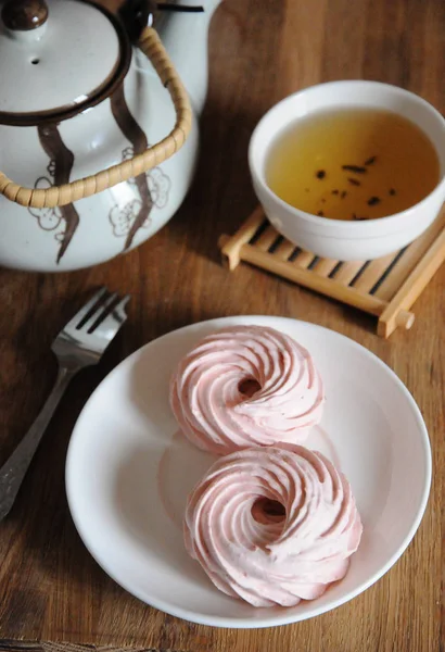 Земляничный зефир на белой тарелке, вилка для десерта, чайник и миска с зеленым чаем — стоковое фото