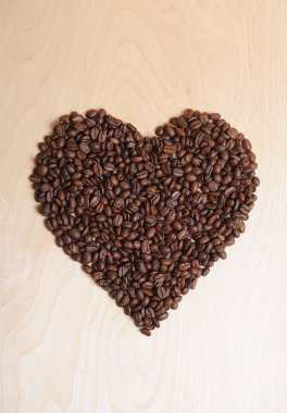 Kahve çekirdekleri hafif ahşap arka plan üzerinde büyük kalp yapılmış