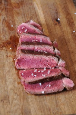 Sığır eti biftek bir ahşap tahta üzerine dilimlenmiş. Kaba tuz serpilir