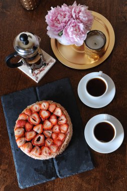 Çilekli cheesecake, kahve kahve makinesi, beyaz bardak, komik vazo, altın şamdan bir tepsi içinde pembe peonies
