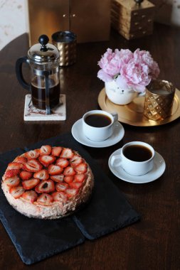 Çilekli cheesecake, kahve kahve makinesi, beyaz bardak, komik vazo, altın şamdan bir tepsi içinde pembe peonies