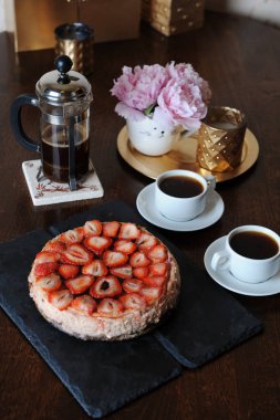 Çilekli cheesecake, kahve kahve makinesi, beyaz bardak, komik vazo, altın şamdan bir tepsi içinde pembe peonies