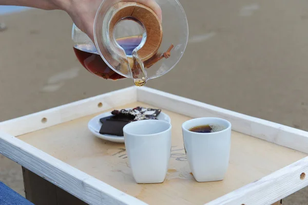 Accesorios para preparar café alternativo en una bandeja en la playa de arena. Barista derrama café en tazas — Foto de Stock