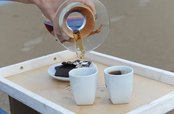 Аксессуары для альтернативного варки кофе на подносе на песчаном пляже. Бариста проливает кофе на чашки — стоковое фото
