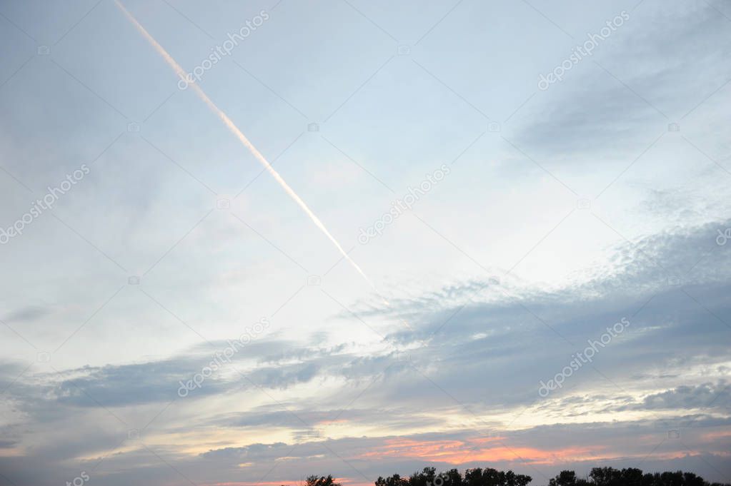 Trail from an airplane in a cloudy blue sky at sunset