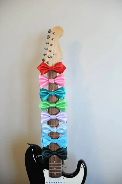 Gravatas de arco multicoloridas em um pescoço de prancha de guitarra. Fundo branco, espaço livre para texto — Fotografia de Stock