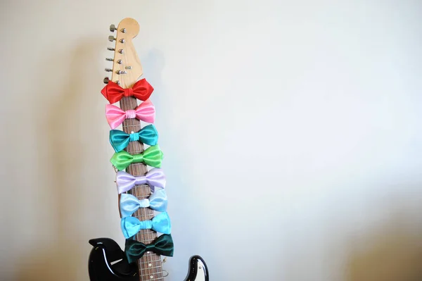 Gravatas de arco multicoloridas em um pescoço de prancha de guitarra. Fundo branco, espaço livre para texto — Fotografia de Stock