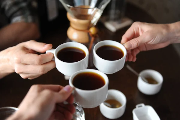 Звон стаканов с тремя чашками кофе на фоне кофейных изделий на дегустации — стоковое фото