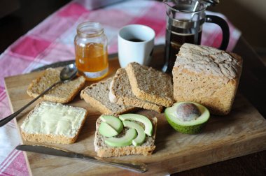 Sağlıklı kahvaltı taze ekmek, kahve, avokado, bal reçel ve ekose masa örtüsü ahşap bir gemide üzerine tereyağı ile