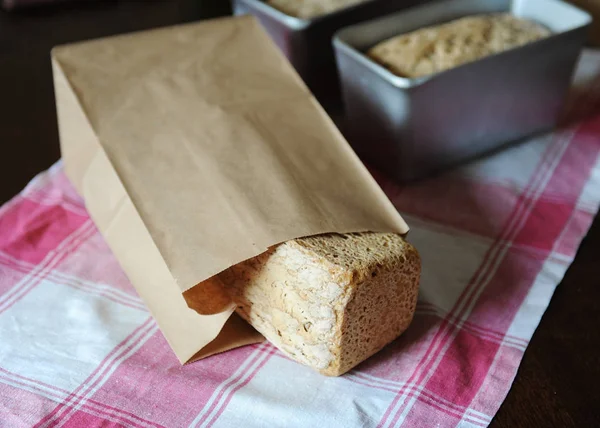 Pan sobre un fermento de centeno sin levadura en una bolsa de papel sobre un mantel a cuadros. Panes en forma de hornear en el fondo —  Fotos de Stock