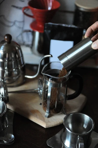 Бариста наливает молотый кофе из кофемолки во французскую прессу. Упаковка с белой этикеткой — стоковое фото