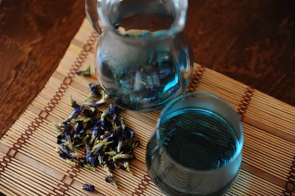 Kruik en glas met blauwe Thaise Anchan thee op bamboe mat op houten tafel. Placer van bloemen voor brouwen, bovenaan weergave — Stockfoto