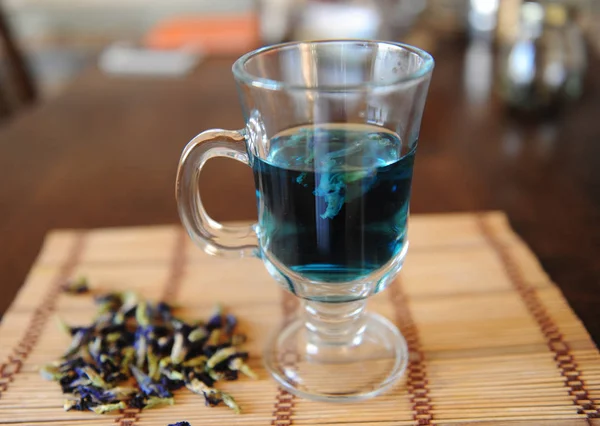 Ancla de té azul tailandés en taza de vidrio sobre estera de bambú sobre mesa de madera. Colocador de flores del clítoris junto a copa — Foto de Stock